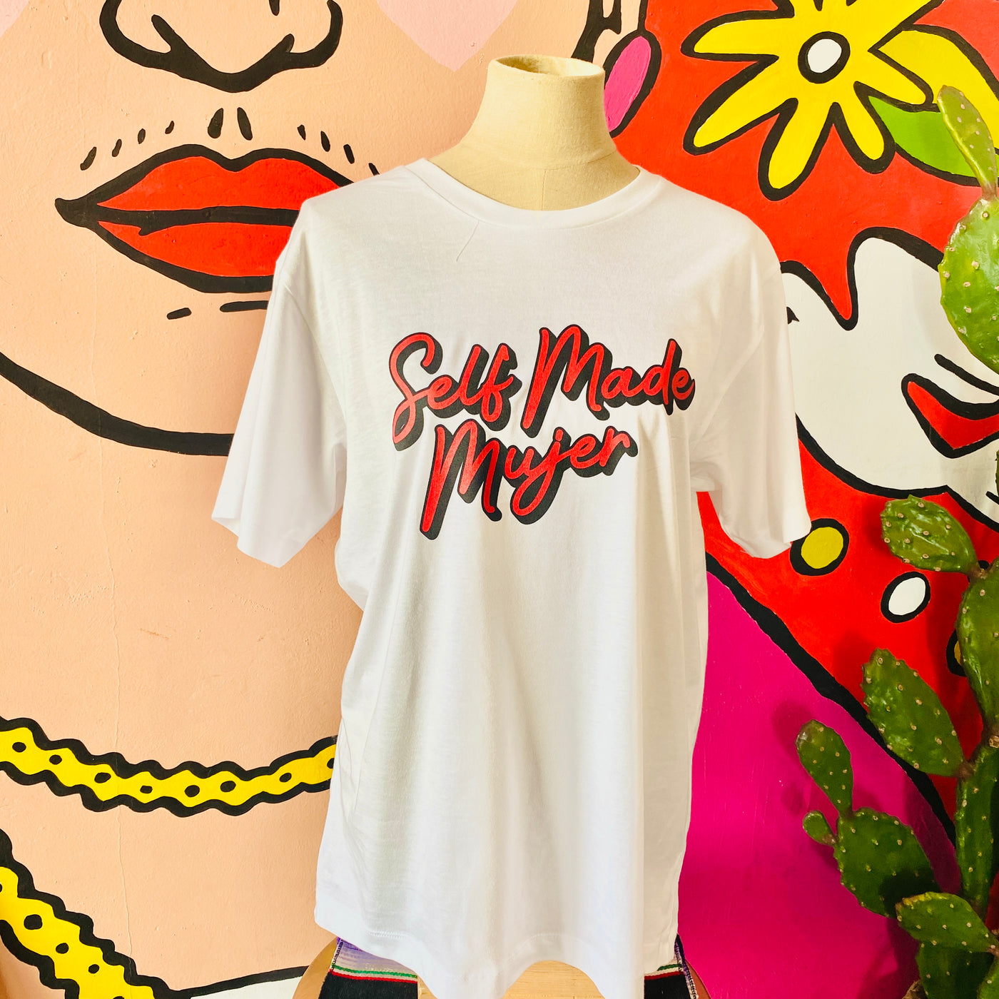 White, "Self Made Mujer" phrase t-shirt with red detail pictured on mannequin. 