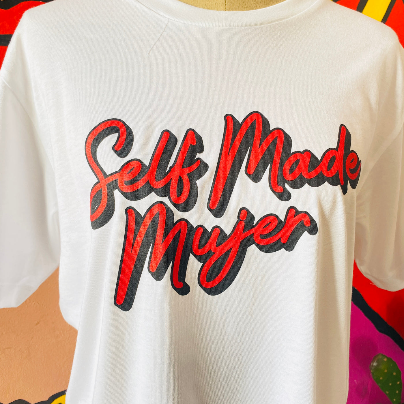 Close up of white, "Self Made Mujer" phrase t-shirt with red detail.