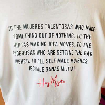 Back of white, "Self Made Mujer" phrase t-shirt with red detail. Back reads, "To the mujeres talentosas who make something out of nothing. To the mijitas making jefa moves. To the poderosas who are setting the bar higher. To all self made mujeres, echale ganas mijita!"