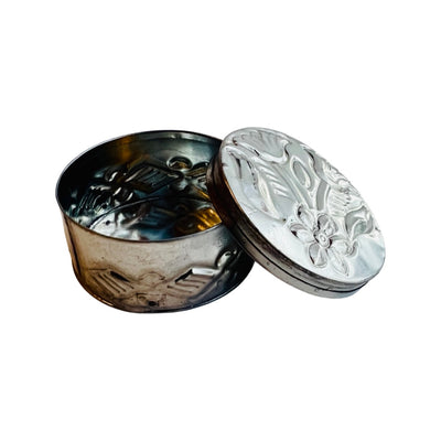 Top view of an opened round tin trinket container with a hammered flower design on the lid.