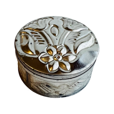 Round tin trinket container with a hammered flower design on the lid.