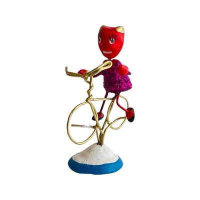 Side view of a painted clay devil with a glittery torso on a bike made of wire. 