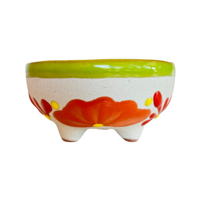 Front view of a ceramic molcajete painted with a lime green rim and orange blossom.