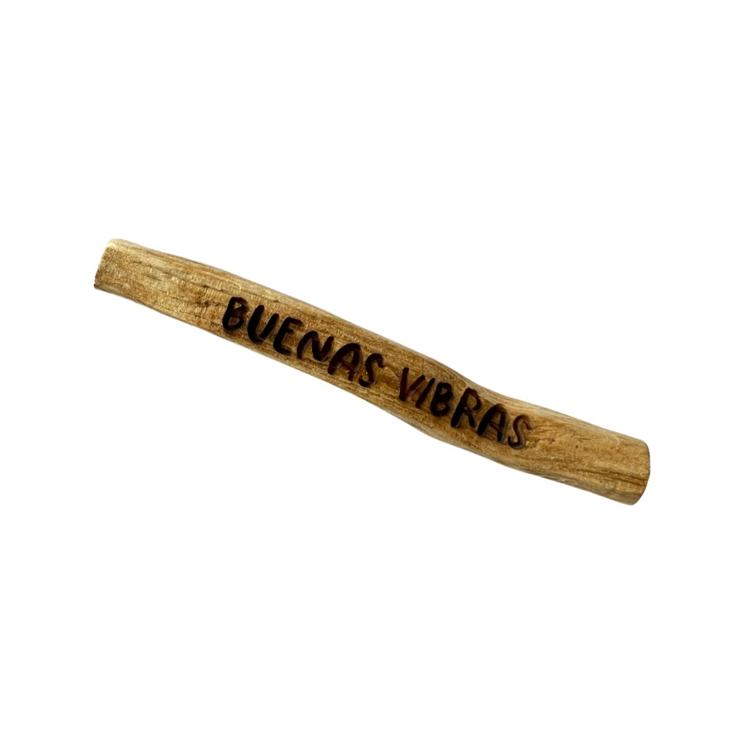 A single stick of palo santo with the phrase Buenas vibras engraved onto it. Translation: Good vibes